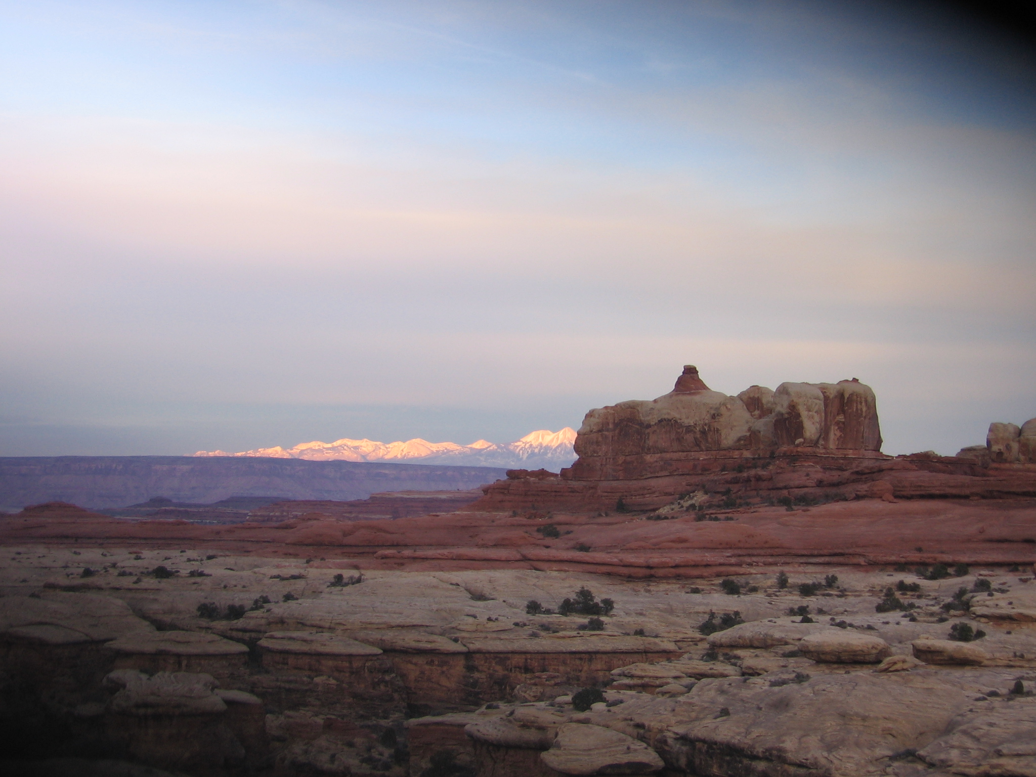 shiny La Sal mountains in the distance behind a big rock outcropping